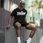 Young man in a Brooklyn Handstyle T-shirt, showcasing urban pride with graffiti-style lettering, sitting on a stone ledge. His casual style embodies city life and cultural expression.