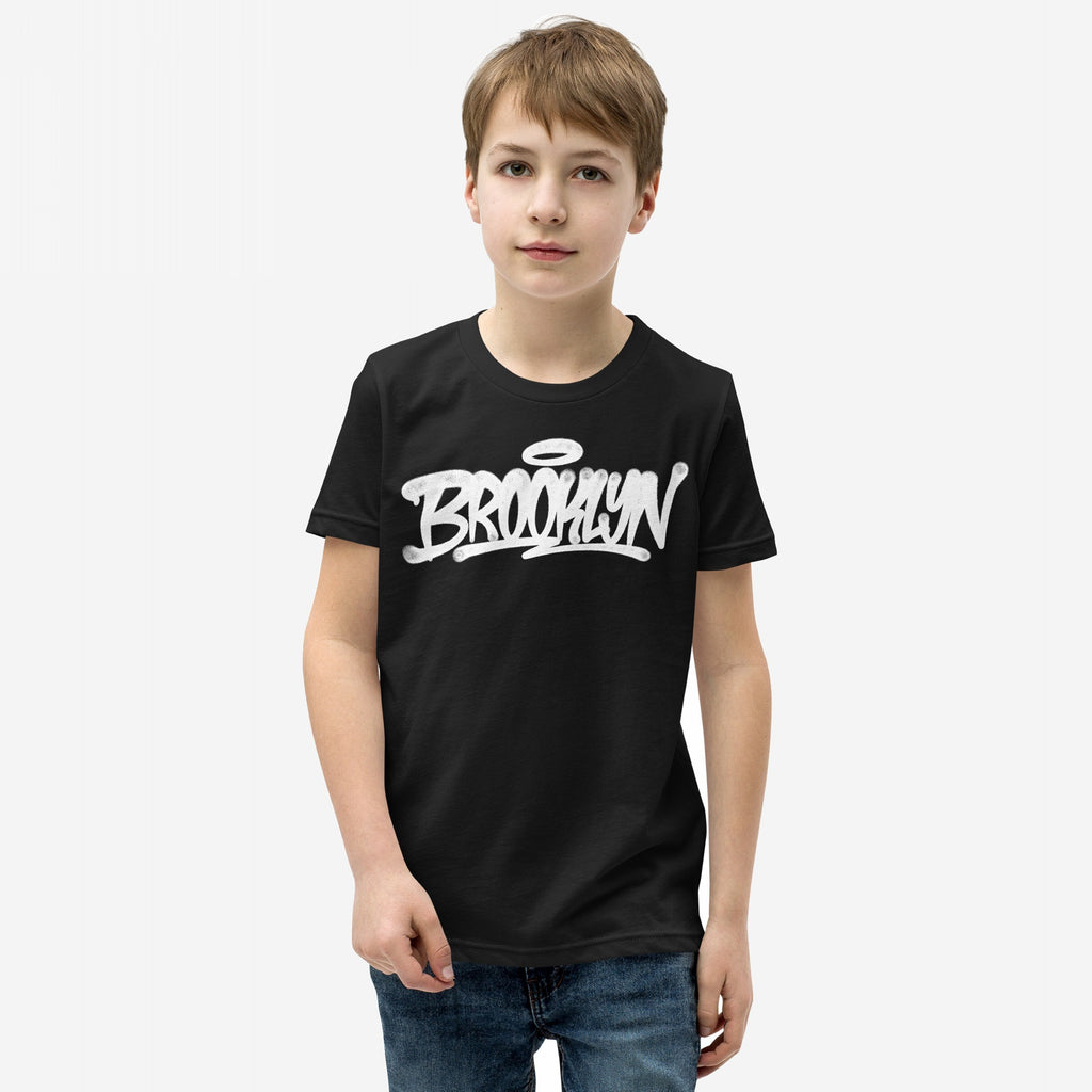 Young boy wearing the Brooklyn Handstyle T-shirt with graffiti-style Brooklyn script and halo accent, embodying everyday borough pride. Suitable for various occasions, from school to city adventures.