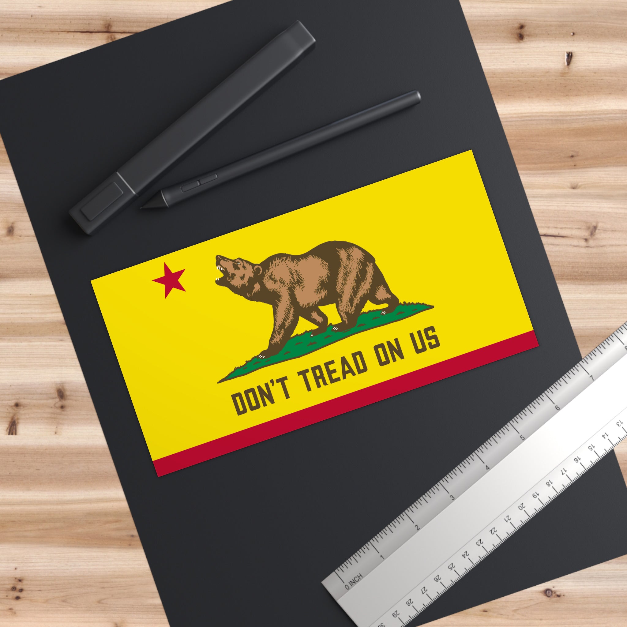 California Gadsden Flag Sticker & Magnet featuring a bear with “Don’t Tread on Us” slogan, lay on a dark mat with a pen and ruler, symbolizing protest and California pride.