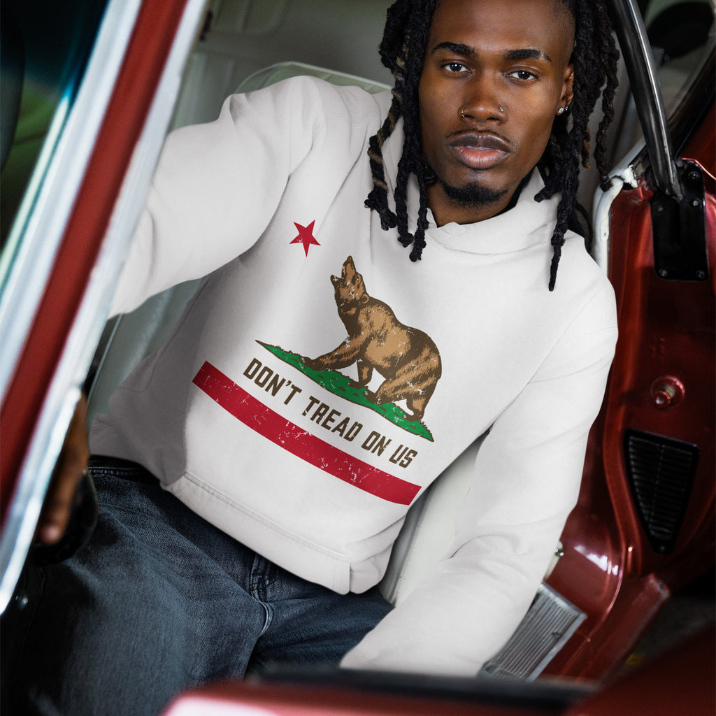 Young man with dreadlocks in a vintage car wears the California Gadsden Flag Shirt featuring a bear and DON'T TREAD ON US slogan, embodying protest and pride.