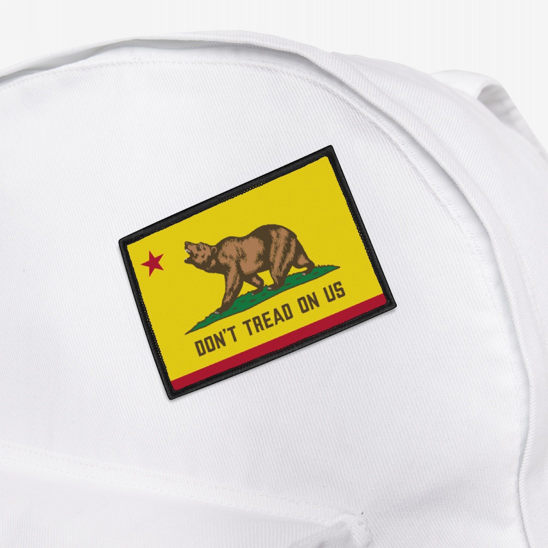 California Gadsden Flag Patch on a white canvas backpack, featuring a brown bear on green grass with a red star. The bold text reads “DON’T TREAD ON US” against a yellow background.