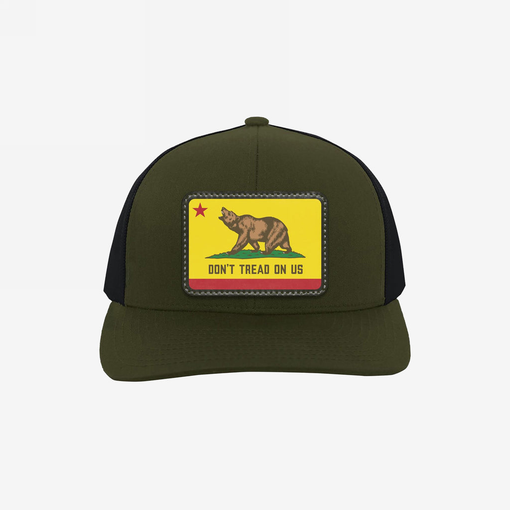 California Gadsden Flag Trucker Hat with an olive front and black mesh back. Features a leatherette patch with a bear and the phrase “DON’T TREAD ON US,” symbolizing defiance and unity.