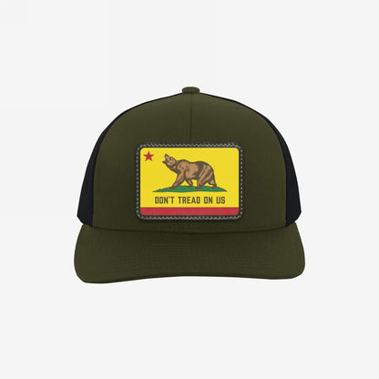 California Gadsden Flag Trucker Hat with an olive front and black mesh back. Features a leatherette patch with a bear and the phrase “DON’T TREAD ON US,” symbolizing defiance and unity.