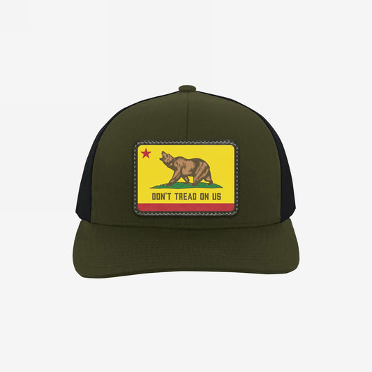 California Gadsden Flag Trucker Hat with an olive front and black mesh back. Features a leatherette patch with a bear and the phrase “DON’T TREAD ON US,” symbolizing defiance and unity.