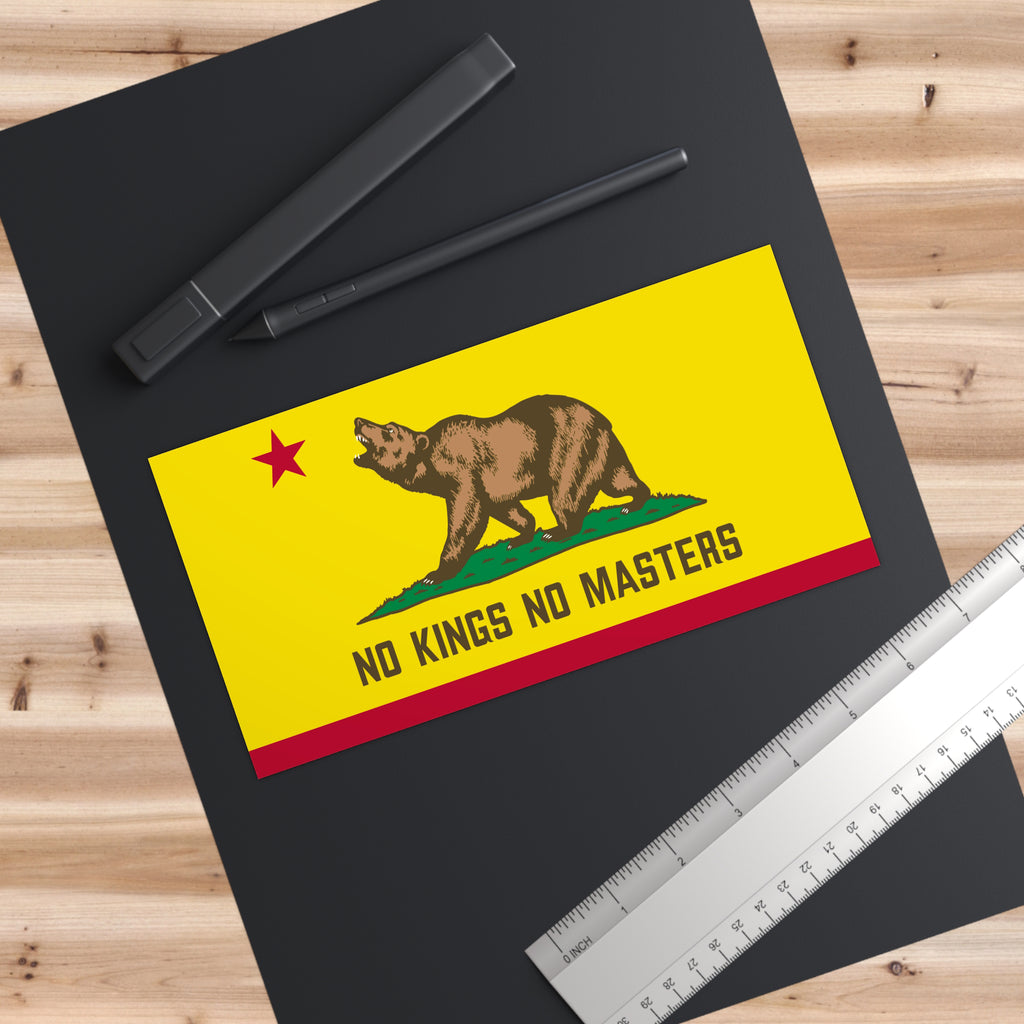 California Flag No Kings Sticker & Magnet features a brown bear on a yellow card with NO KINGS NO MASTERS, symbolizing resistance. Accompanied by pens and a ruler on a desk.