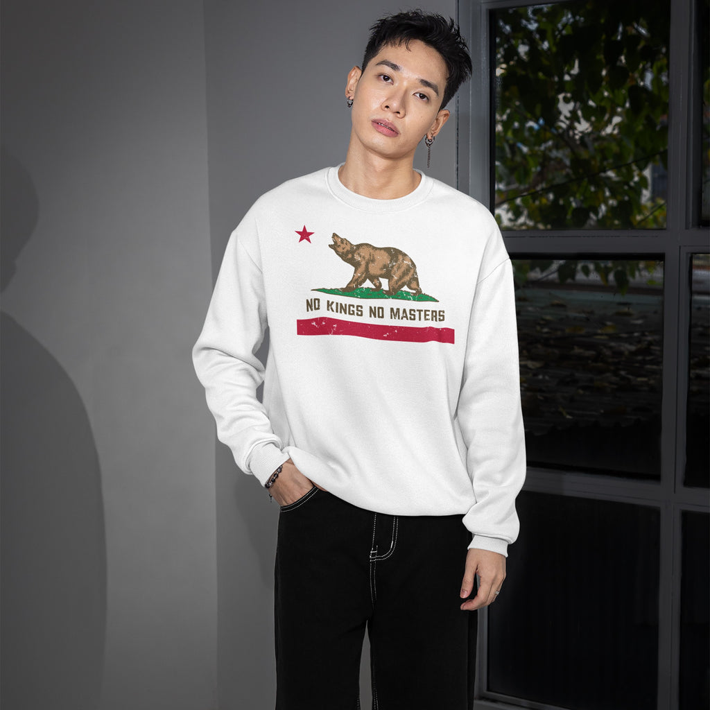 Young man in a white California No Kings Flag Shirt, featuring a roaring bear design and text advocating autonomy, stands by a window in a minimalist room, embodying bold rebellion and equality.