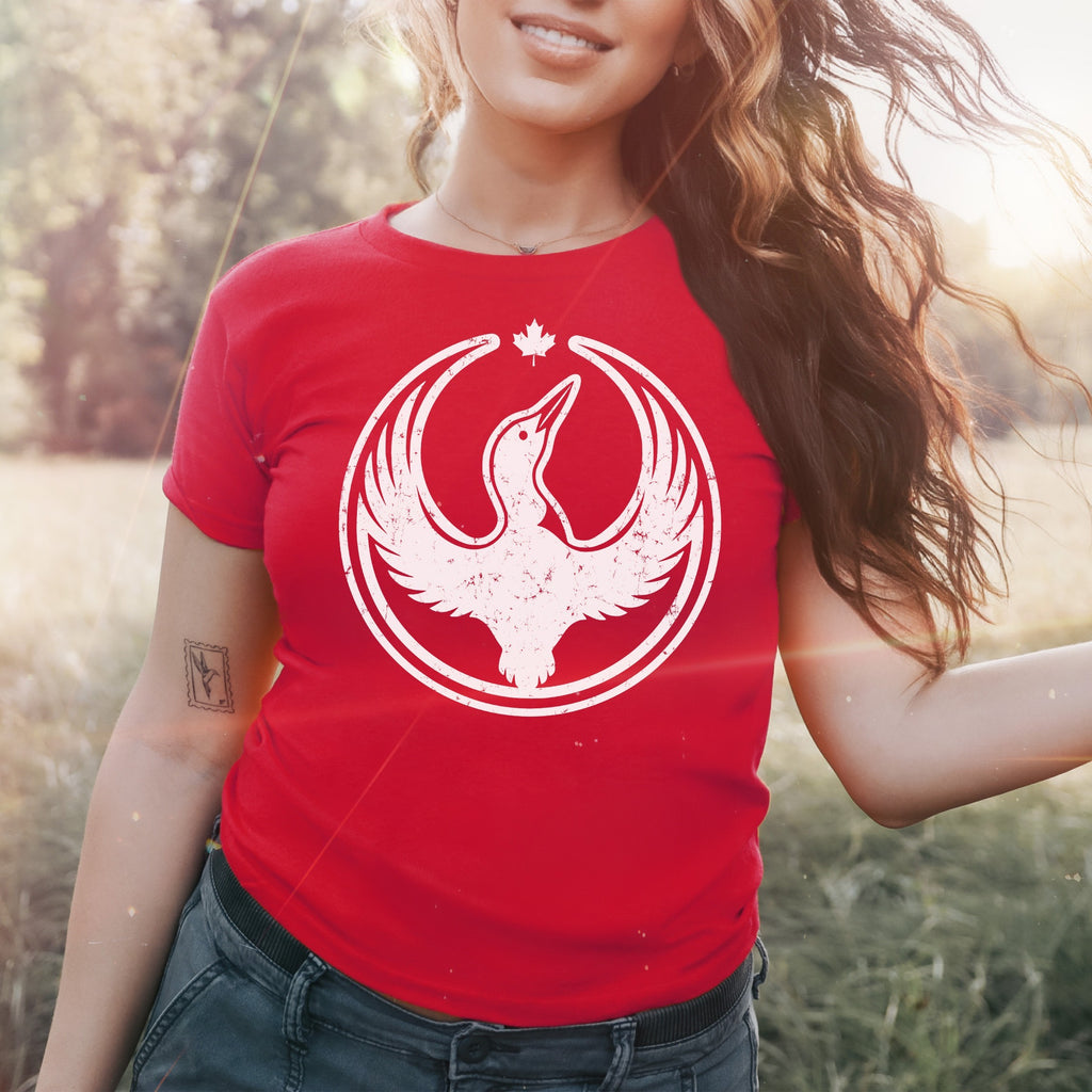 Person in a field wearing the Canada Rebel Alliance Women's Baby Tee, featuring a distressed white loon and maple leaf graphic, embodying anti-fascist and equality values, with a relaxed, summery ambiance.