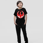 Young boy in a Canada Rebel Alliance T-shirt, featuring a red phoenix emblem and maple leaf, represents a powerful anti-fascist and equality message. Hands in pockets, neutral expression.