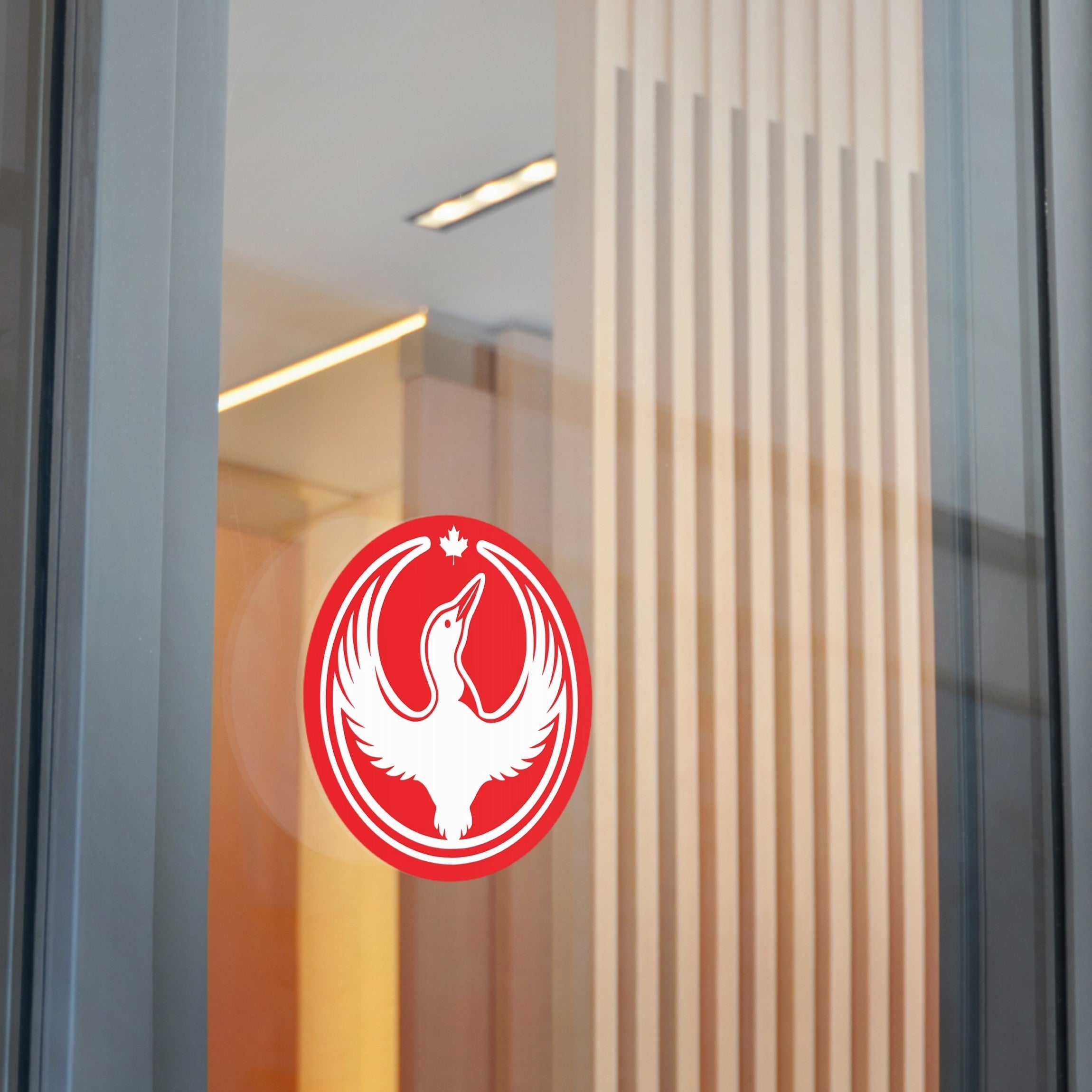 Canada Rebel Alliance Sticker on glass, showcasing a white bird in a red-and-white emblem with a maple leaf above. The background features warm-toned wood slats and modern lighting, symbolizing bold protest art.