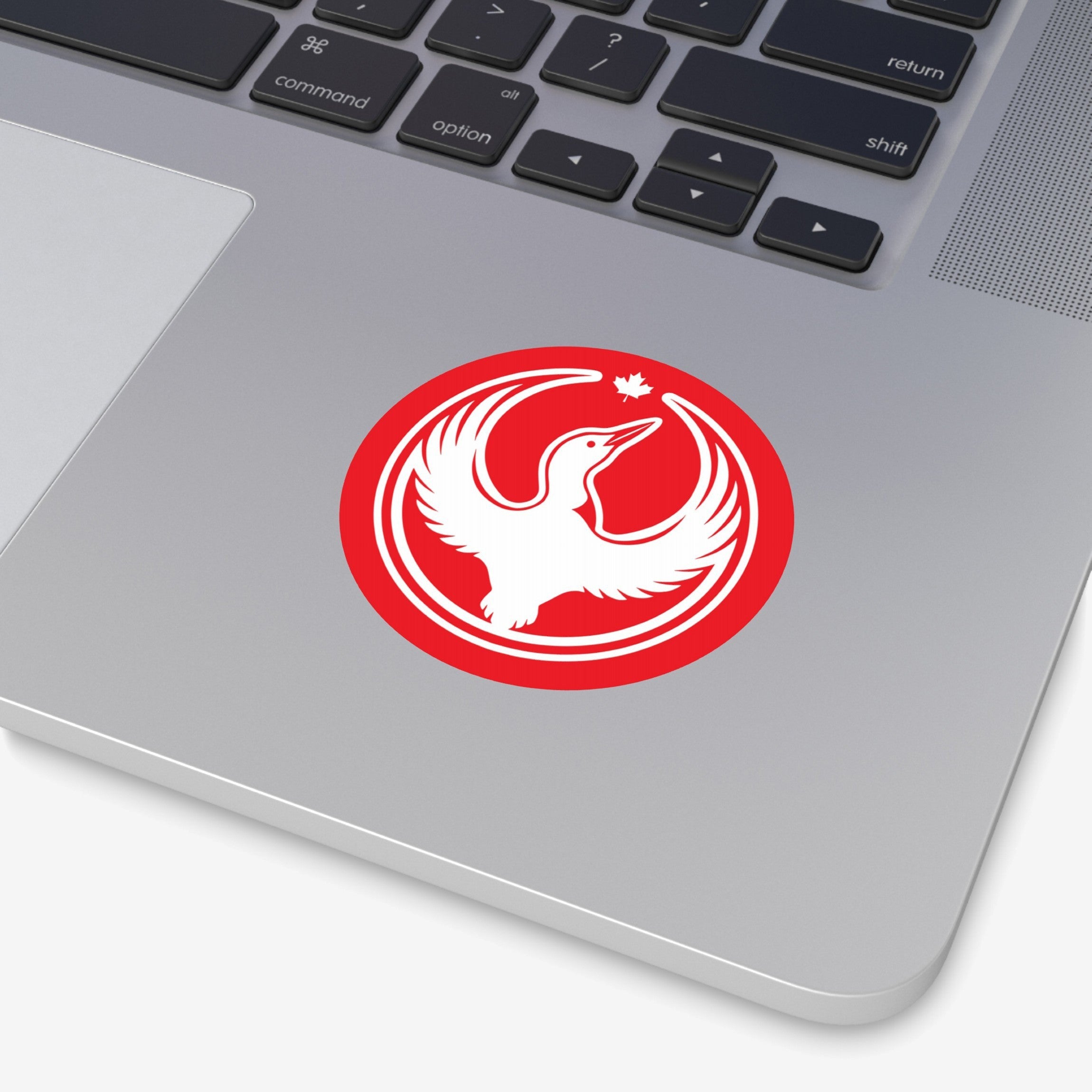 Close-up of a MacBook with the Canada Rebel Alliance Sticker, featuring a white bird in flight and a maple leaf, symbolizing anti-fascism and community support, placed below the keyboard.