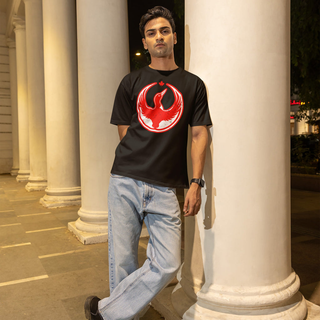 Young man at night wearing a Canada Rebel Alliance T-shirt with a red bird emblem, leaning against a column, showcasing a design symbolizing anti-fascist protest and support for equality.