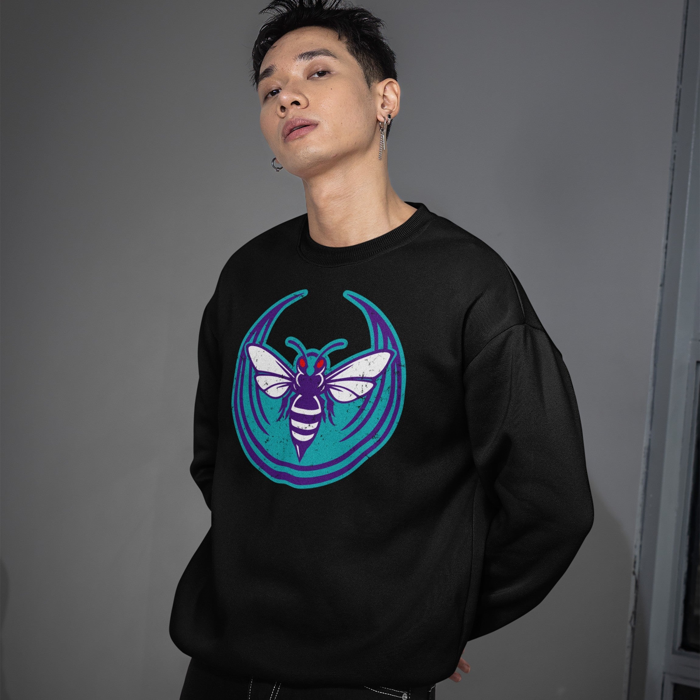 Young man in a black crewneck sweatshirt featuring the Charlotte Rebel Alliance design with a stylized bee graphic in purple, white, and teal, embodying a bold, anti-fascist statement.