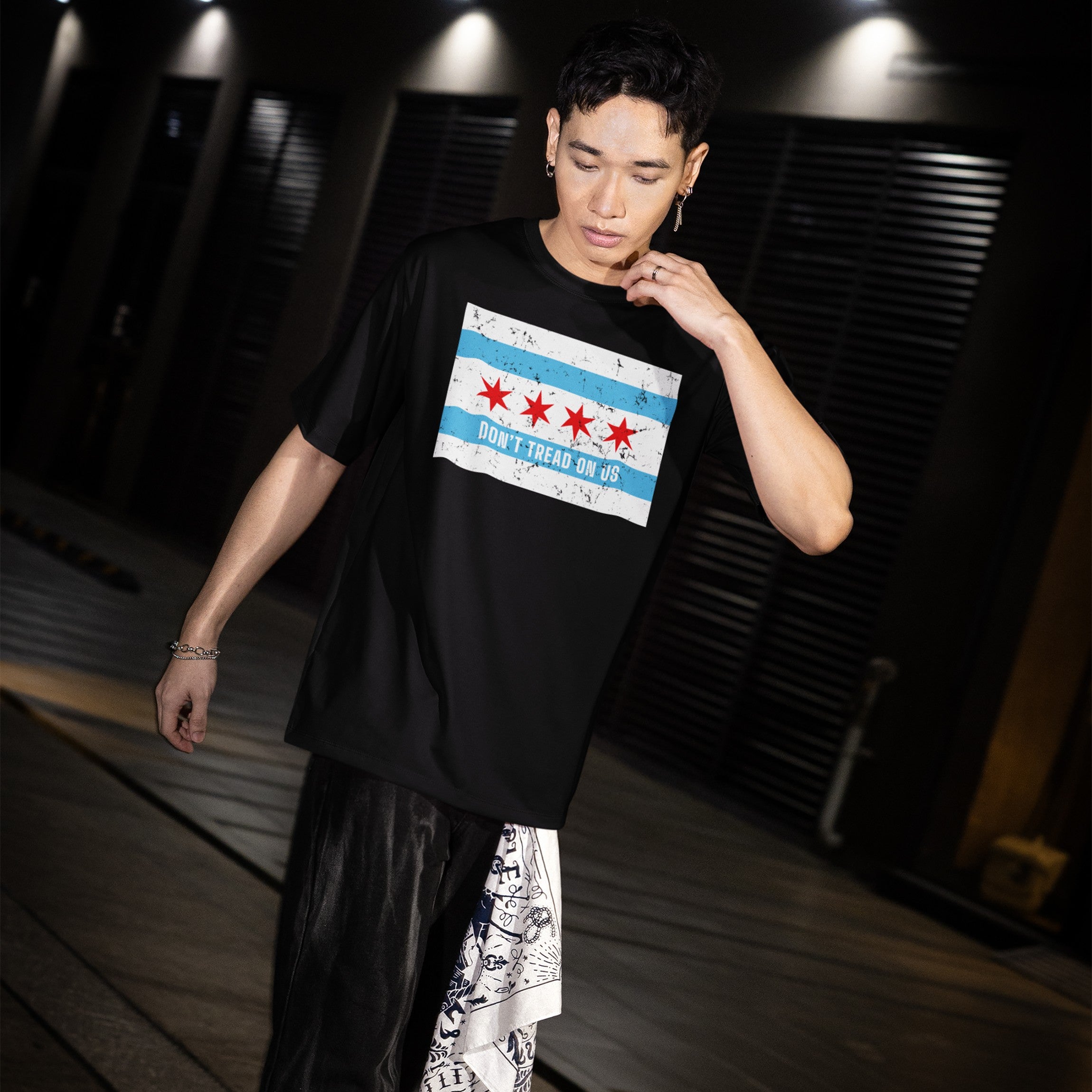 Young man wearing the Chicago Gadsden Flag Shirt with the city's flag and DON’T TREAD ON US slogan, embodying resistance and activism, walking through an urban corridor at night.