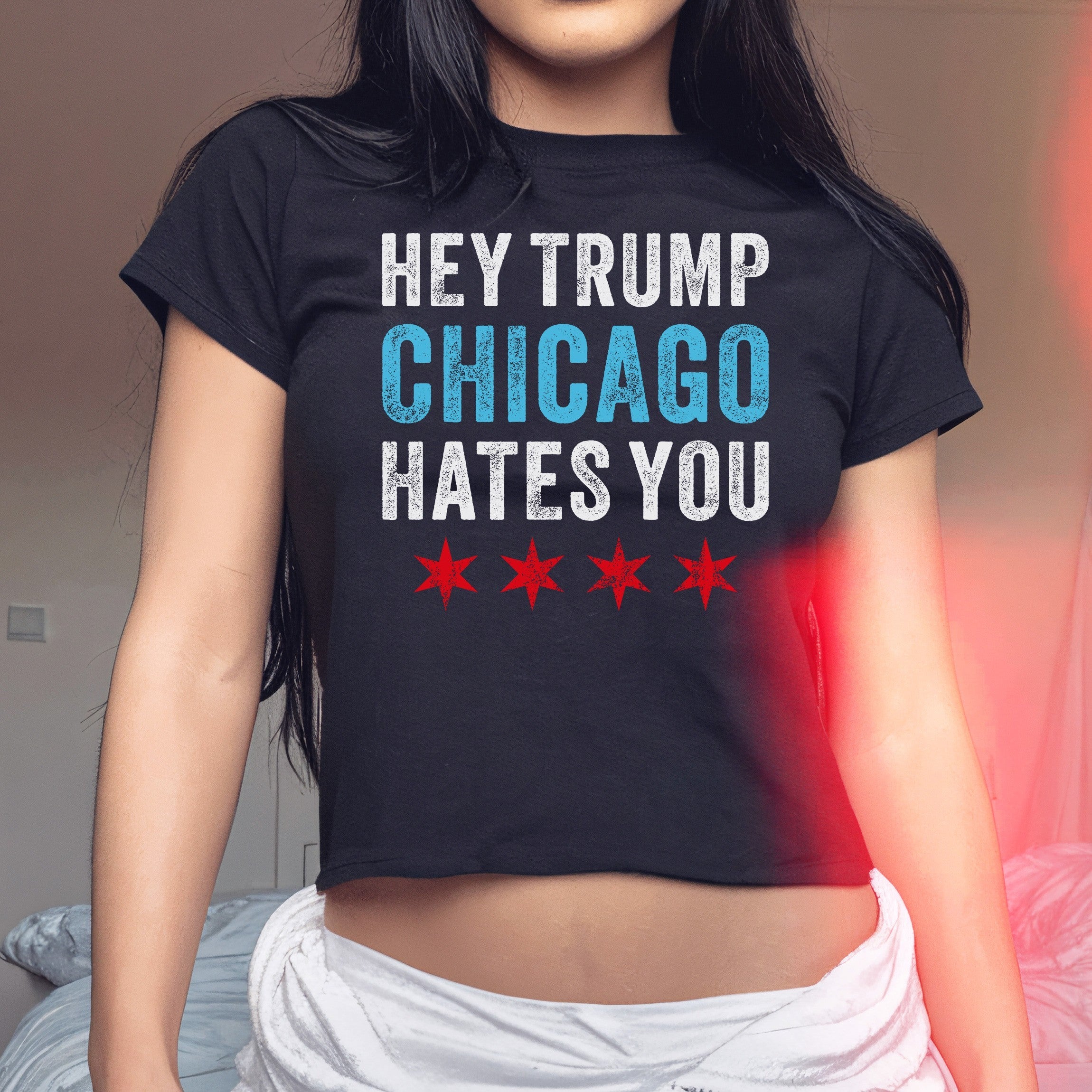 Chicago Hates Trump Women's Baby Tee features a bold slogan and four stars, worn by a woman indoors, highlighting a statement piece for those voicing opposition and supporting equality.