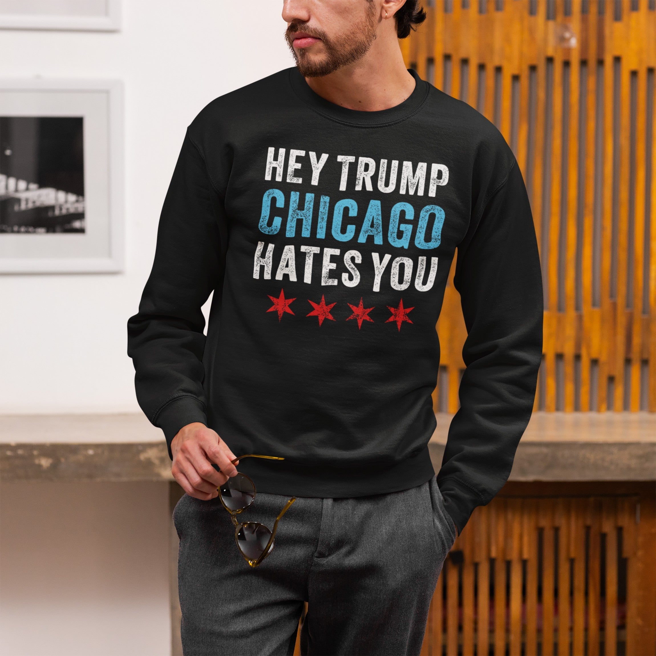 Chicago Hates Trump Hoodie & Sweatshirt features a bold protest slogan with Chicago flag stars, worn by a man indoors, embodying the spirit of civic pride and resistance.