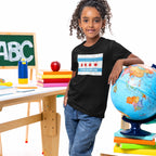 Young girl in a classroom setting wears the Chicago No Kings Flag Shirt, featuring a city-flag design and phrase NO KINGS NO MASTERS, symbolizing freedom and defiance.