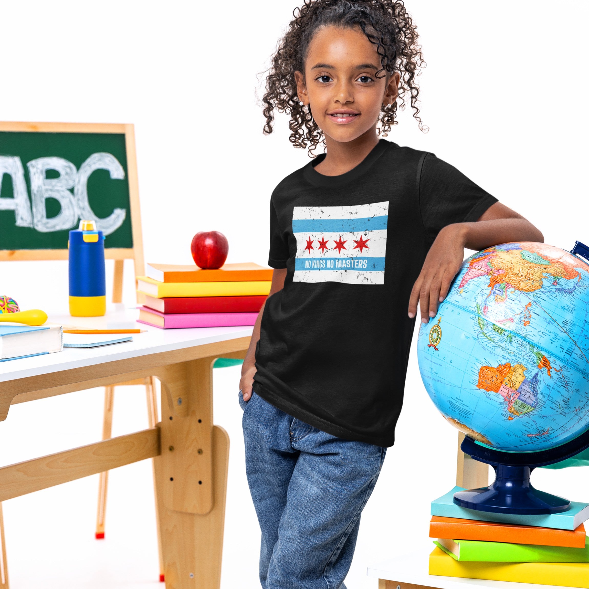 Young girl in a classroom setting wears the Chicago No Kings Flag Shirt, featuring a city-flag design and phrase NO KINGS NO MASTERS, symbolizing freedom and defiance.