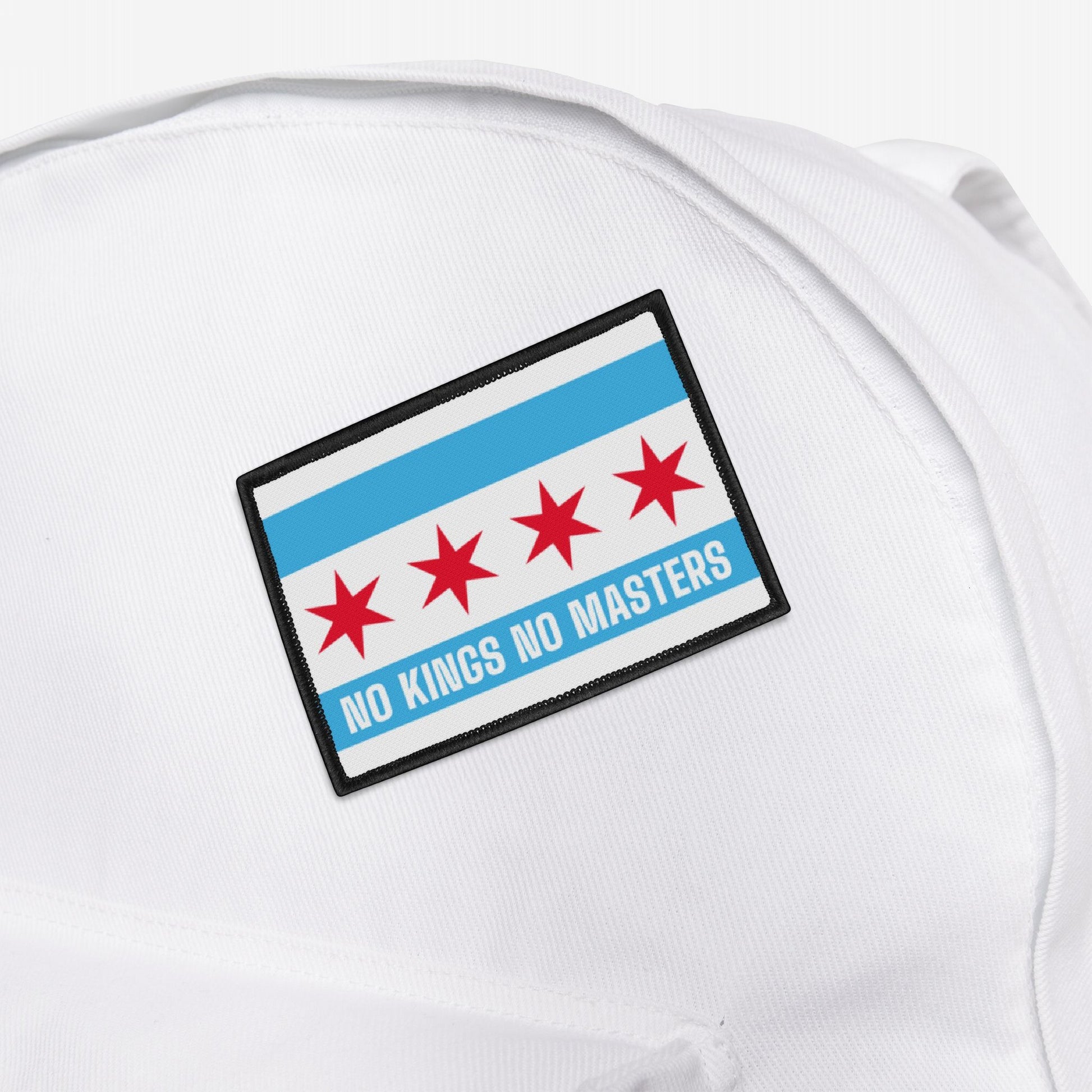 Chicago Flag No Kings Patch on a white fabric surface, featuring the reimagined city flag with anti-authoritarian message, NO KINGS NO MASTERS, in bold white letters on a light-blue stripe.