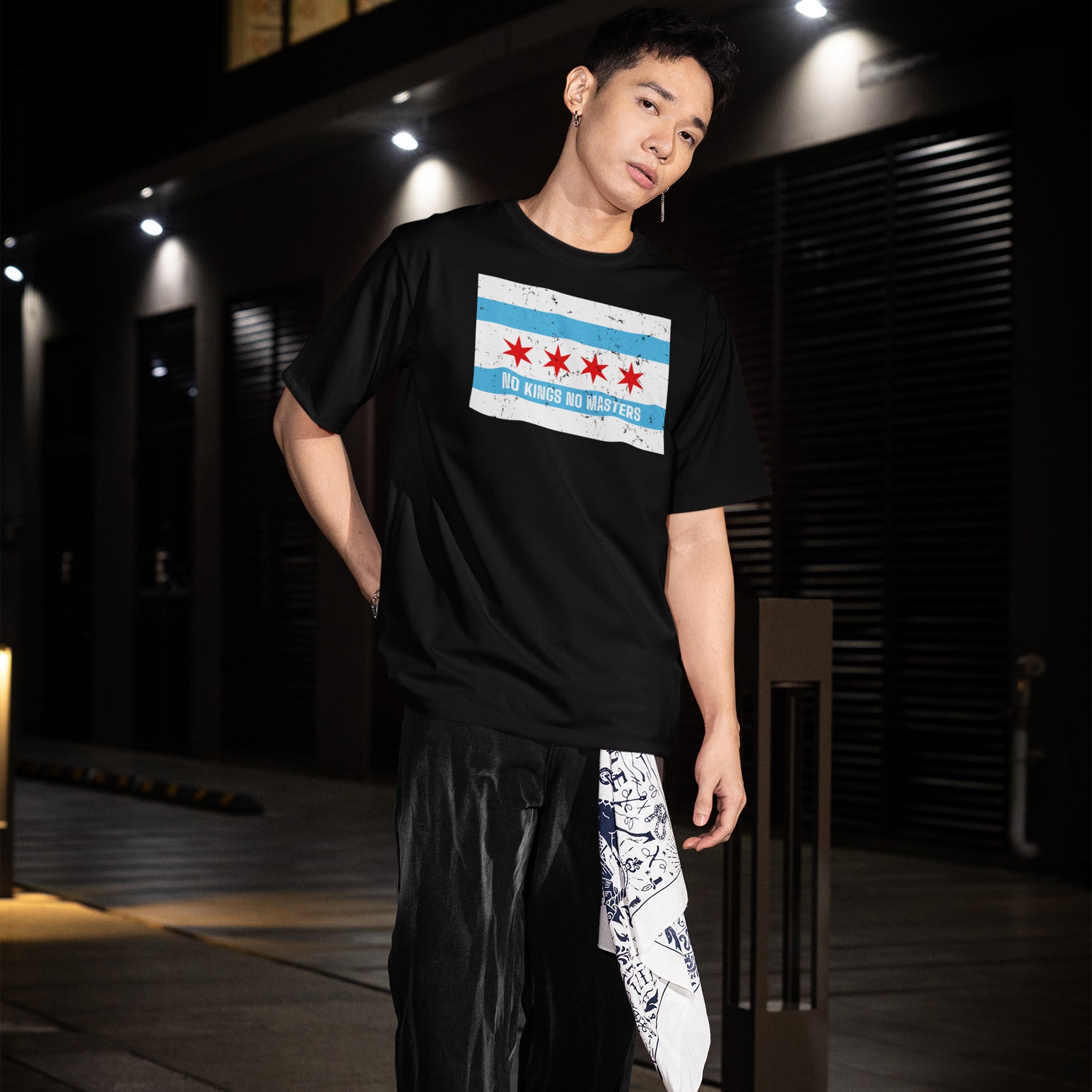 Young adult wearing the Chicago No Kings Flag Shirt with the city's flag and anti-authoritarian slogan, paired with dark pants and a patterned bandana, embodying local rebellion and equality.