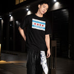 Young adult wearing the Chicago No Kings Flag Shirt with the city's flag and anti-authoritarian slogan, paired with dark pants and a patterned bandana, embodying local rebellion and equality.