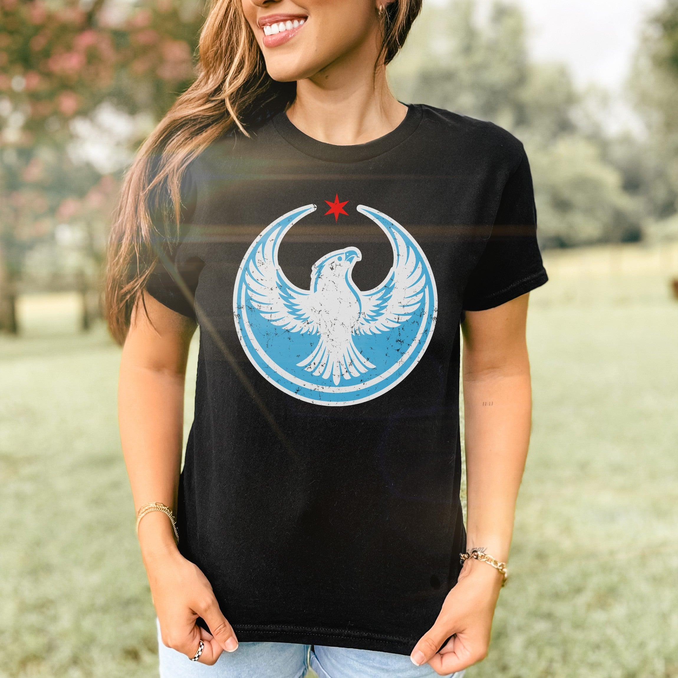 Chicago Rebel Alliance Women's Baby Tee featuring a white peregrine falcon in a light blue circle with a red star. Modeled outdoors, this tee exemplifies bold activism and Chicago pride.
