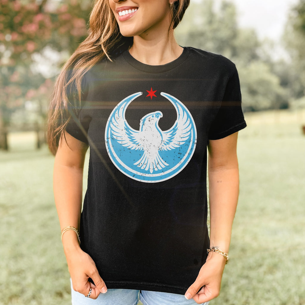 Chicago Rebel Alliance Women's Baby Tee featuring a white peregrine falcon in a light blue circle with a red star. Modeled outdoors, this tee exemplifies bold activism and Chicago pride.