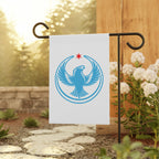 Chicago Rebel Alliance Garden Flag on a black metal stand, featuring a blue peregrine falcon emblem with a red star, set in a garden beside a wooden post and white flowering shrubs.