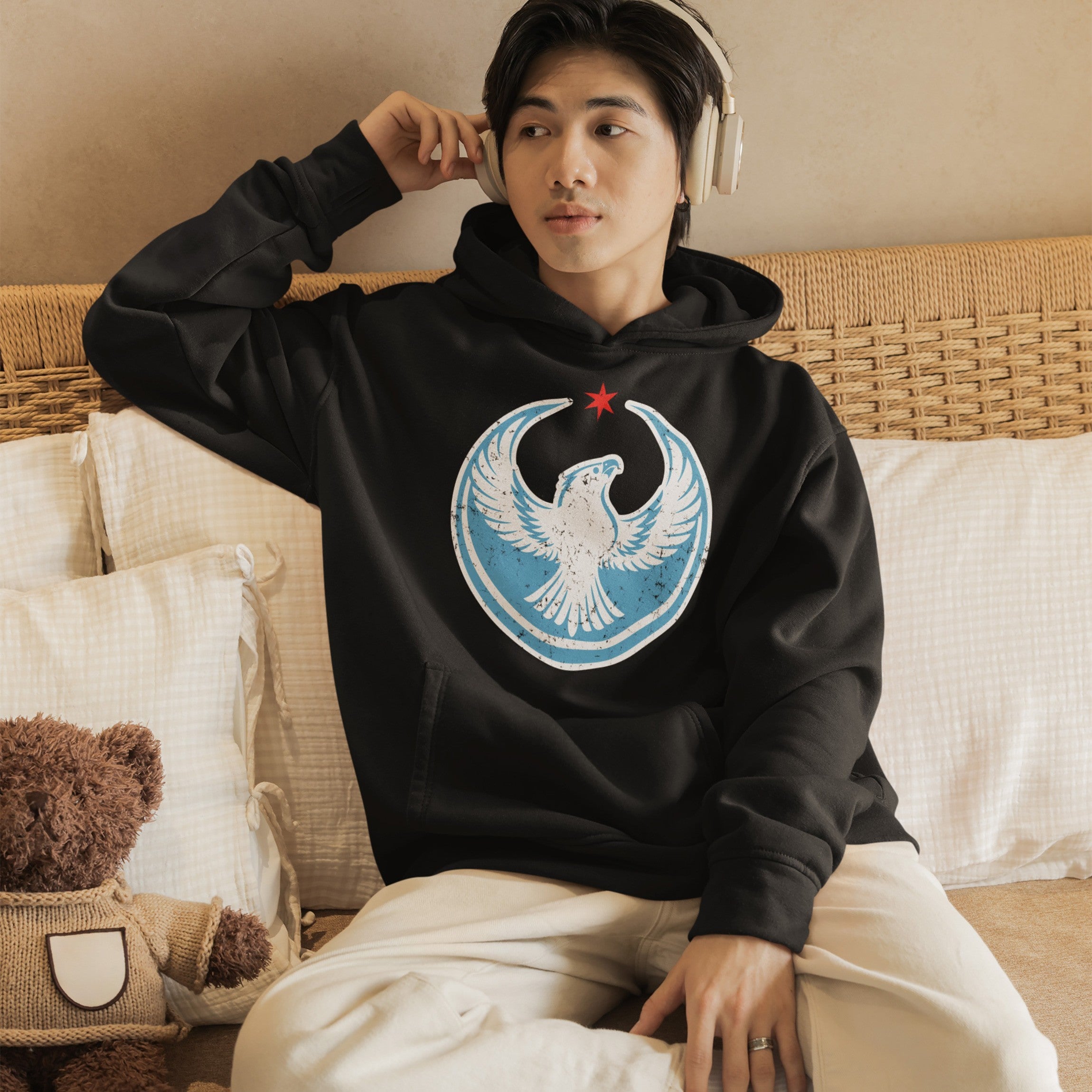 Chicago Rebel Alliance Hoodie features a stylized eagle crest with a red star, worn by a young person on a cozy bed, embodying a relaxed yet defiant stance against neutrality.