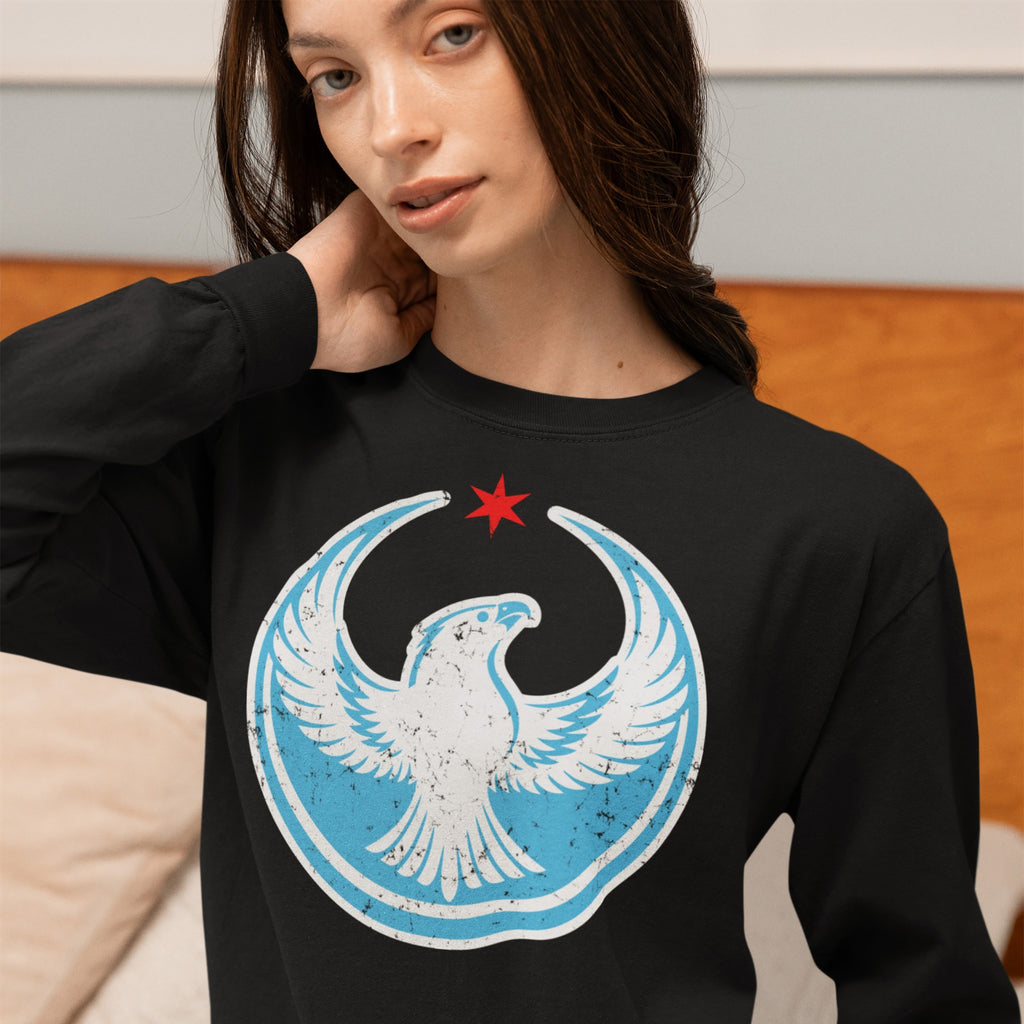 Young woman wearing the Chicago Rebel Alliance T-shirt, featuring a distressed-style white peregrine falcon emblem with a red star, symbolizing anti-fascist and immigrant rights support, in a relaxed home setting.