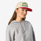 Young woman wearing the Chinga La Migra Hat, featuring a bold anti-fascist slogan in green Gothic lettering, paired with a light gray hoodie against a white background, embodying a defiant protest style.