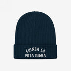 Chinga La Migra Hat: Dark navy-blue knit beanie with a folded cuff, featuring CHINGA LA PUTA MIGRA in white old-English–style embroidery, embodying an anti-fascist statement against ICE and CBP.