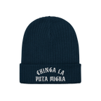 Chinga La Migra Hat: Dark navy-blue knit beanie with a folded cuff, featuring CHINGA LA PUTA MIGRA in white old-English–sty