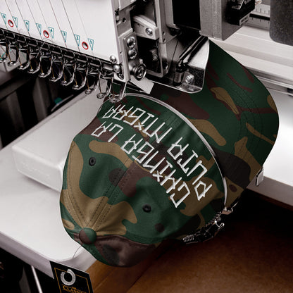 Camouflage-pattern baseball cap, Chinga La Migra Hat, being embroidered with bold white letters on an industrial machine, showcasing a powerful message against oppression, with CLASSIC tag on the brim.