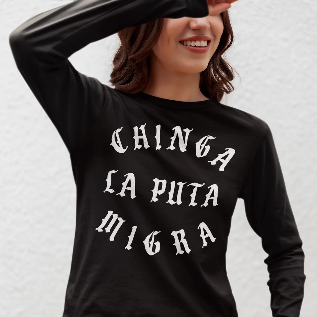 Young woman in a black Chinga La Migra T-shirt, featuring bold, Gothic-style white text promoting anti-fascist messages. She shields her eyes playfully, embodying a spirit of protest and unity.