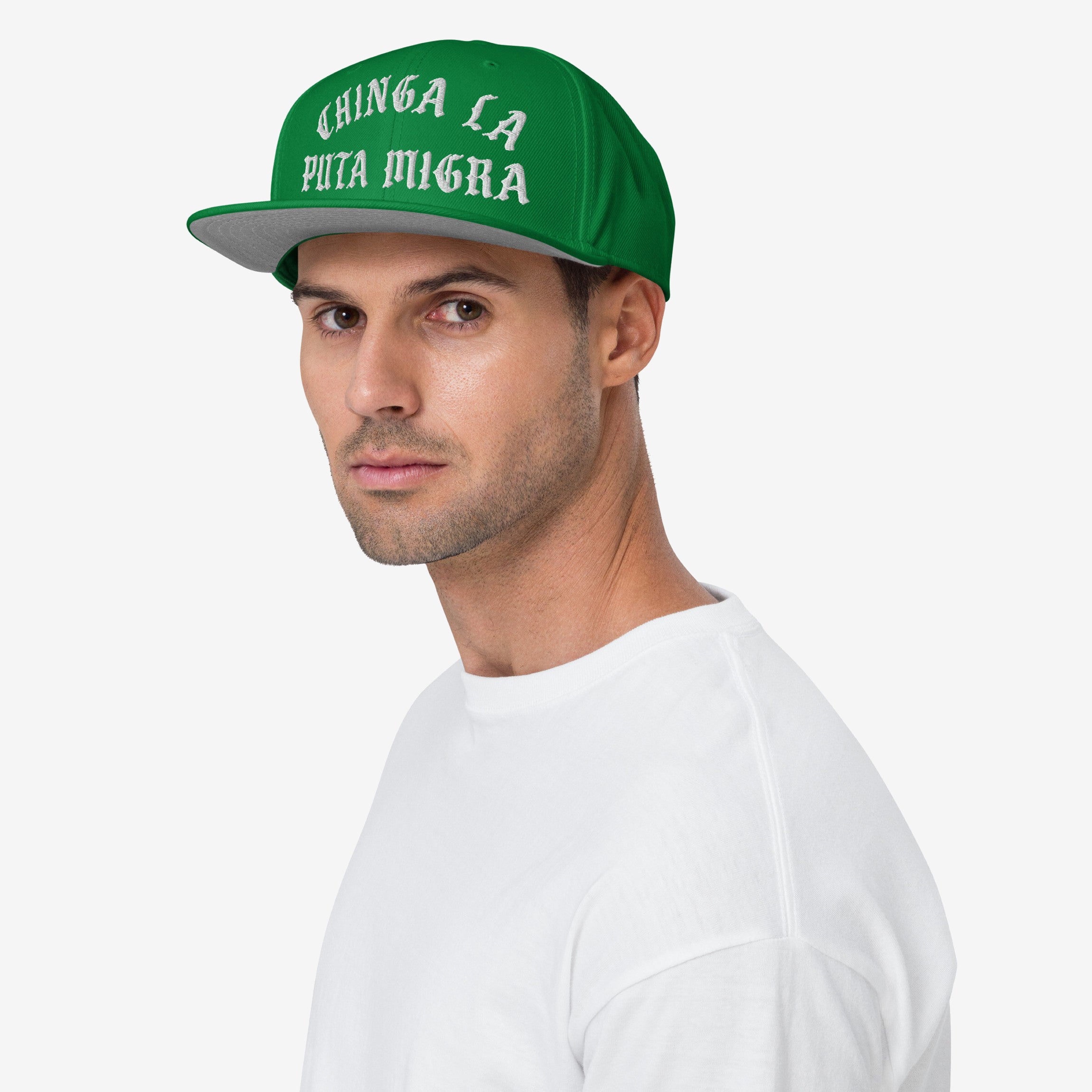 Young man wearing the Chinga La Migra Hat, a green snapback cap with bold, white Gothic-style lettering, representing an anti-ICE message. Perfect for those advocating immigrant rights and equality.