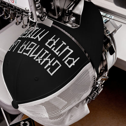Close-up of Chinga La Migra Hat being embroidered on an industrial machine, showcasing the bold block-style lettering on a black front panel with white mesh back, symbolizing resistance against oppression.