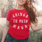 Young woman wearing the Chinga Tu MAGA Women's Baby Tee in bright red, featuring white Gothic-style lettering, standing outdoors in sunlight with a warm glow, reflecting a bold, progressive message.