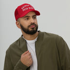 Chinga Tu MAGA Hat featuring bold white Old English-style embroidery on a red trucker cap, worn by a bearded man in an olive-green jacket, symbolizing defiance against fascism and cruelty.