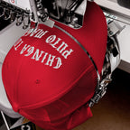 The Chinga Tu MAGA Hat is shown in an embroidery machine, with white thread stitching bold text on the red cap's front, embodying its anti-fascist message.