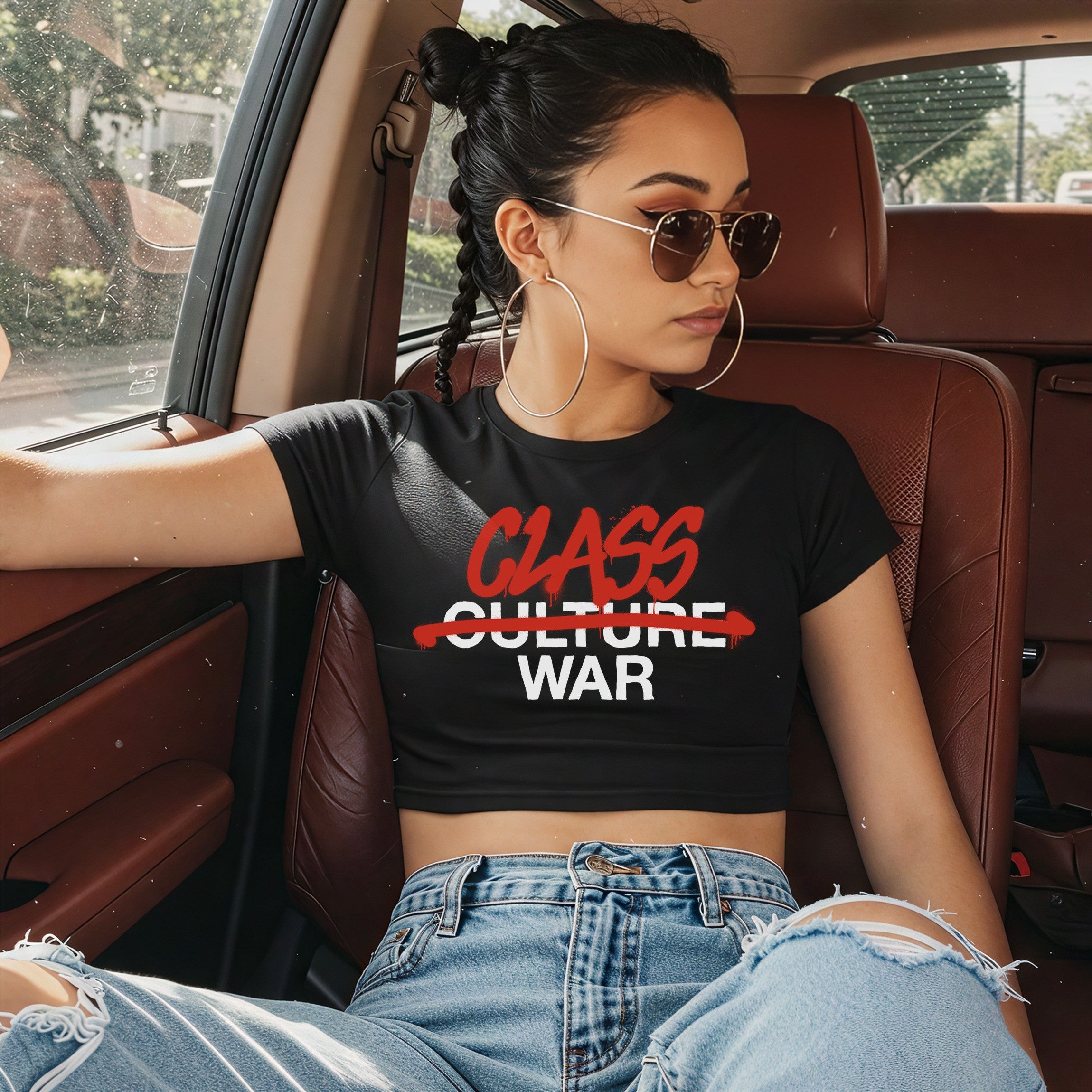 Young woman in a car wears the Class War Women's Baby Tee, featuring bold graffiti-style text CLASS WAR on a black, cropped tee, embodying a statement on social justice and activism.