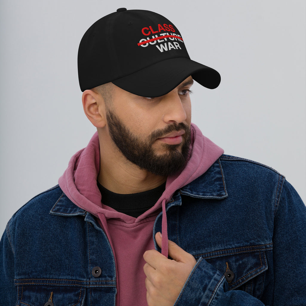 A bearded man models the Class War Hat, featuring bold red and white text highlighting economic justice by crossing out Culture War, emphasizing unity with a denim jacket and hoodie ensemble.