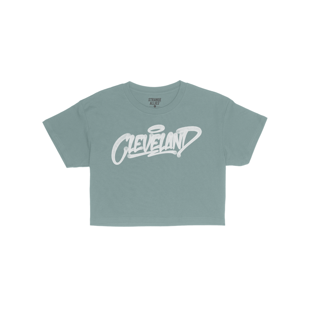 The Cleveland Handstyle Women's Baby Tee in navy blue features a white, graffiti-style Cleveland script with a halo above the