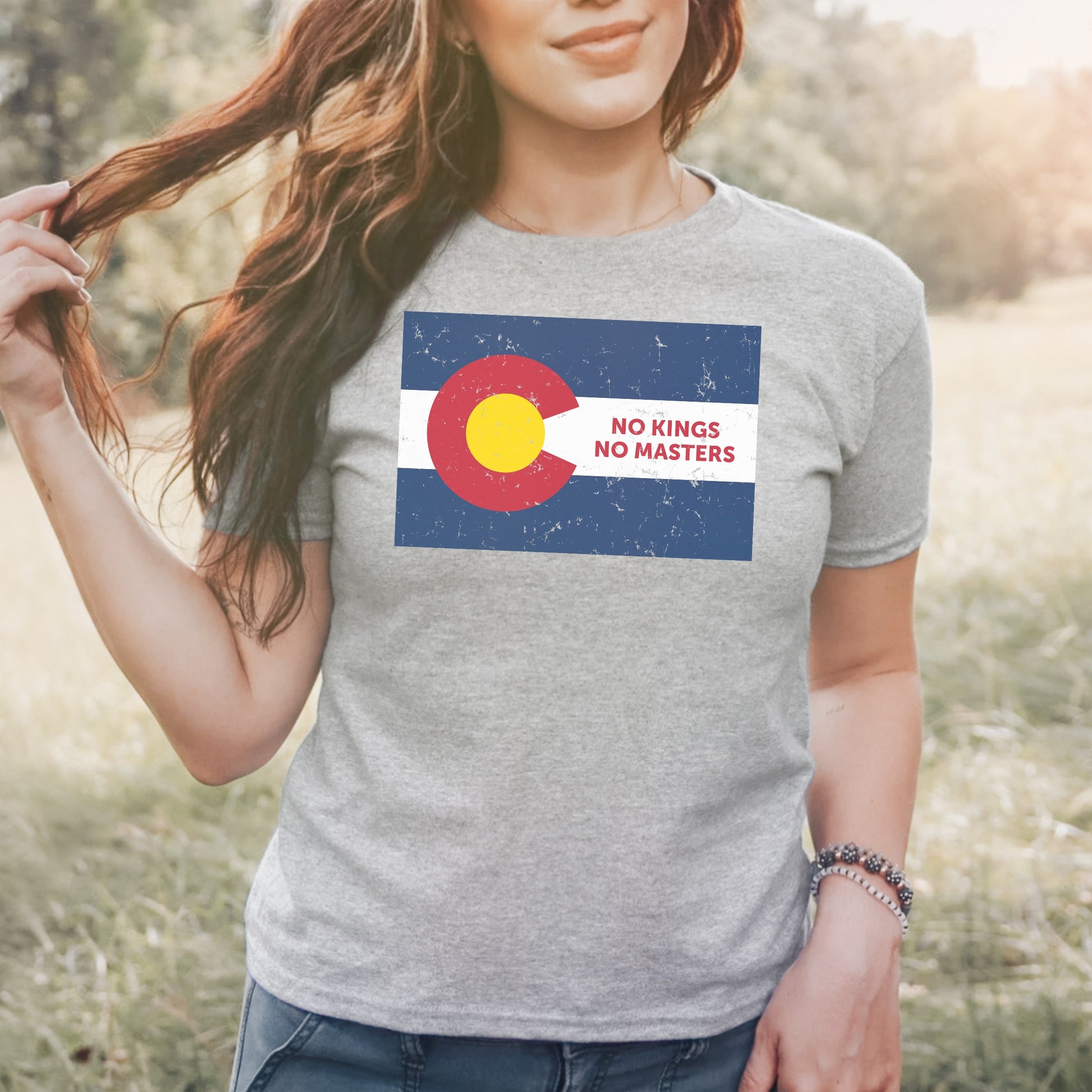 Person wears the Colorado No Kings Flag Women's Baby Tee, featuring a distressed state flag design with bold NO KINGS NO MASTERS text, embodying defiance and resistance against authoritarianism.