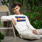 Young man wearing a Colorado No Kings Flag Shirt featuring a stylized Colorado flag design, seated among lush houseplants, embodying a rebellious spirit aligned with the ethos of autonomy and equality.