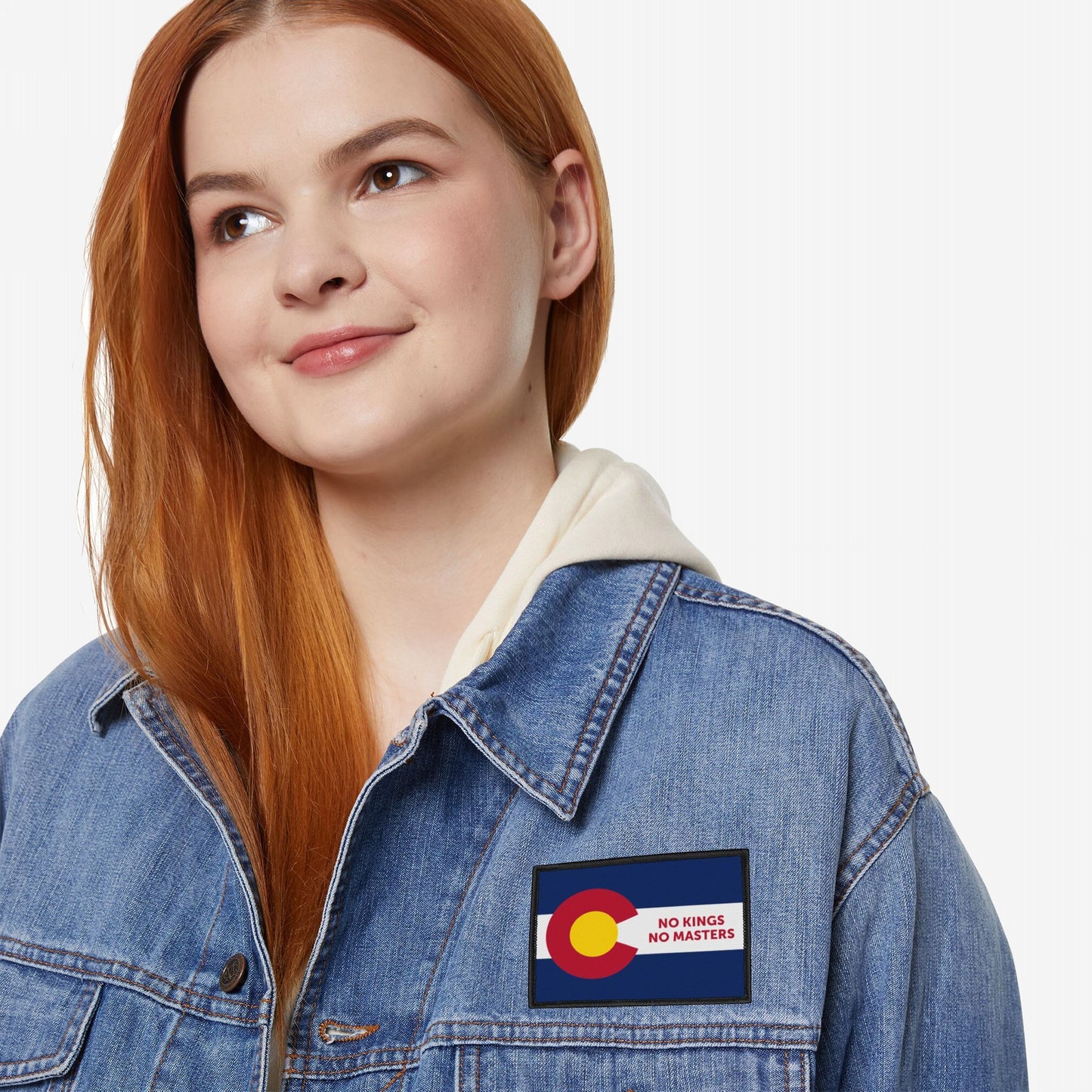 Young woman wears a light wash denim jacket featuring the Colorado Flag No Kings Patch, symbolizing self-governance with NO KINGS NO MASTERS slogan, against a plain white background.