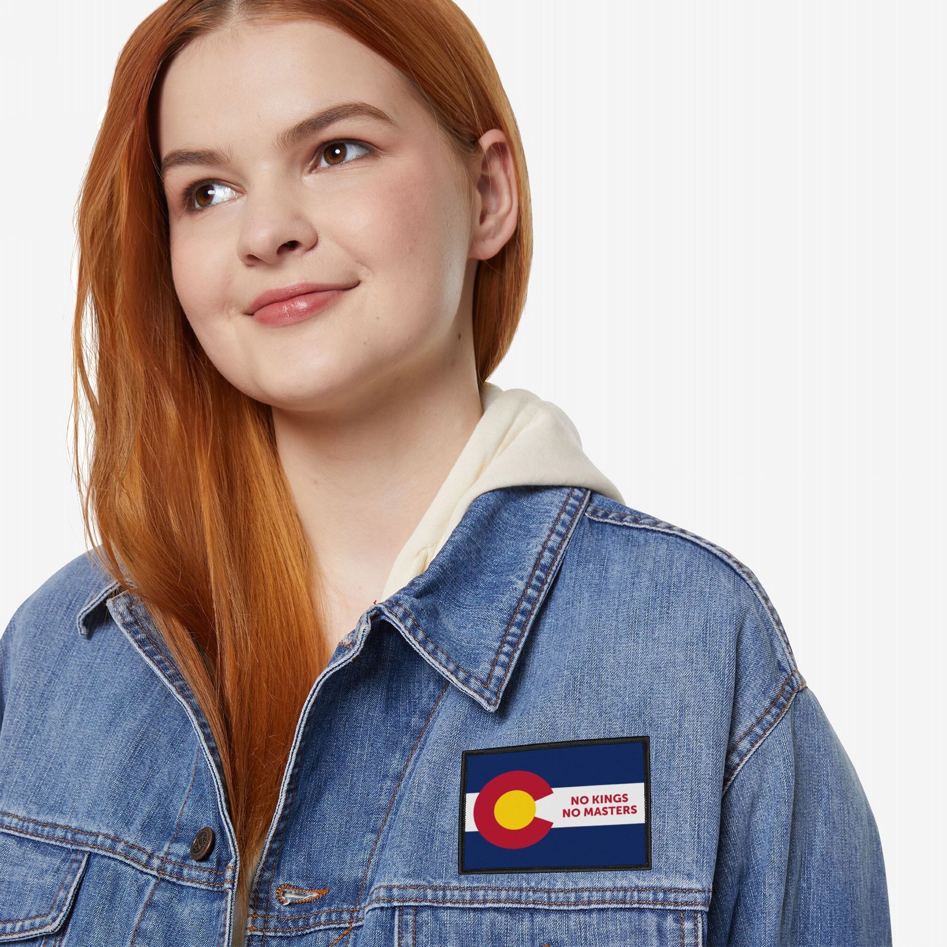 Young woman wears a light wash denim jacket featuring the Colorado Flag No Kings Patch, symbolizing self-governance with NO KINGS NO MASTERS slogan, against a plain white background.