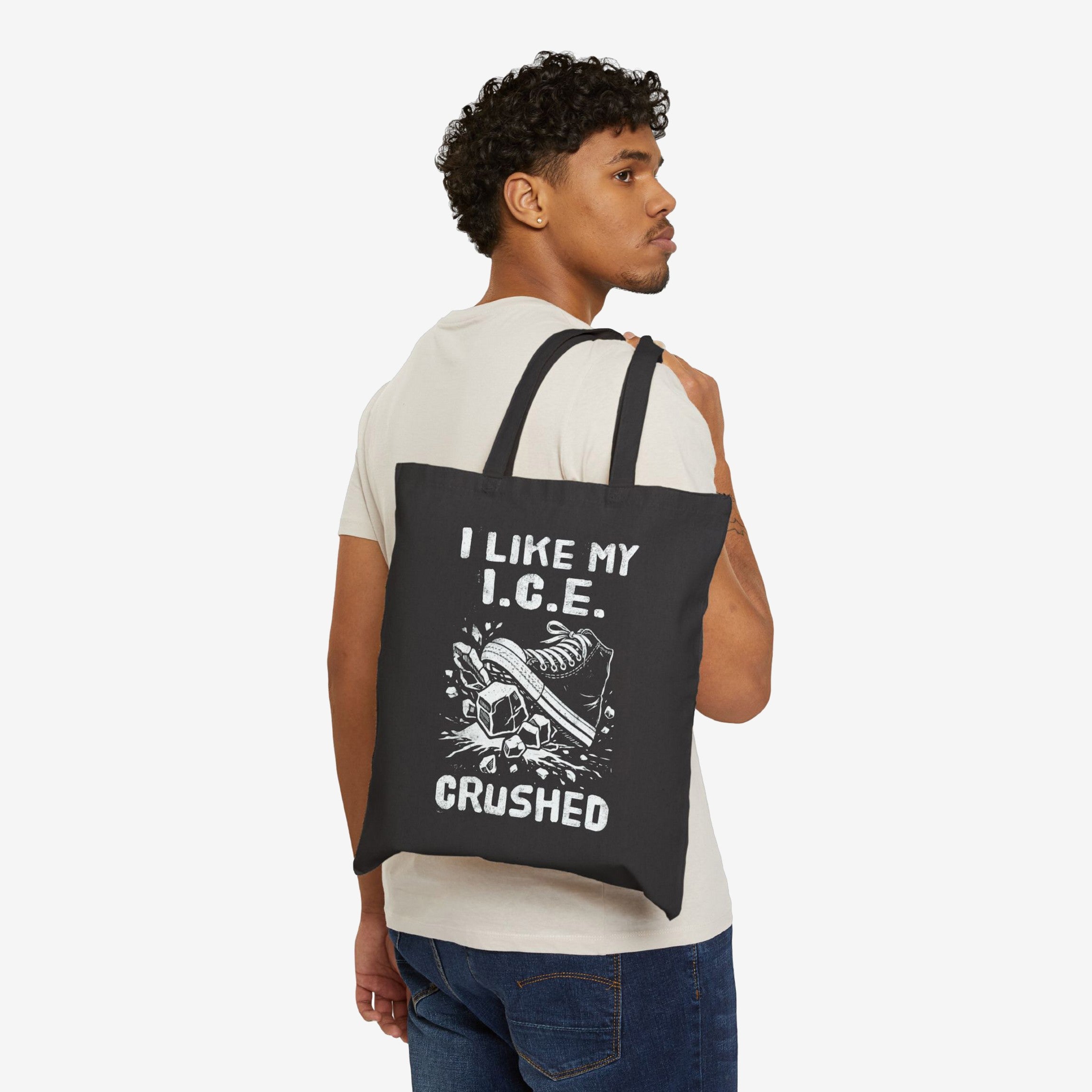 Crushed ICE Tote Bag: Young man in light attire carries a black tote featuring a sneaker crushing ice graphic and slogan, embodying anti-fascist and pro-immigrant rights sentiments, ideal for community supporters.