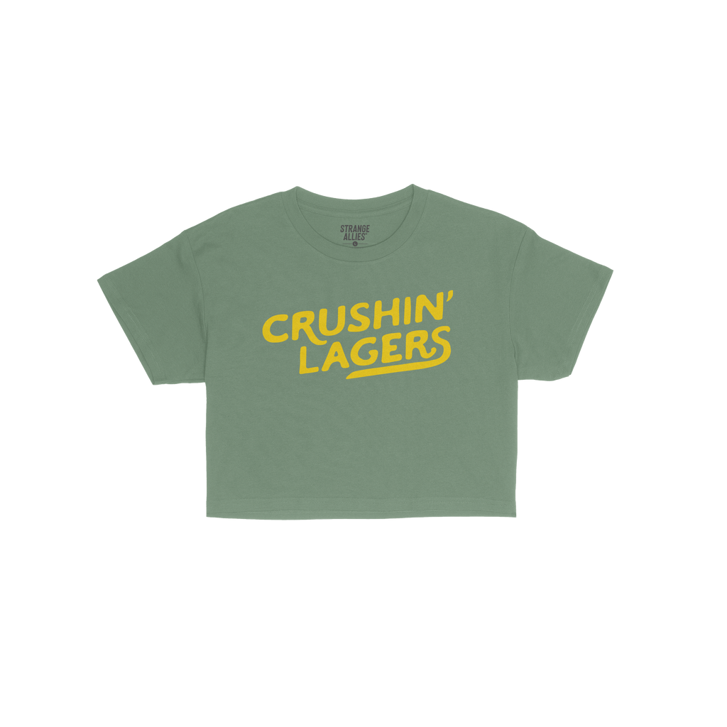 Crushin' Lagers Women's Baby Tee features bold yellow CRUSHIN’ LAGERS text on a green crop top, exuding retro varsity vibes