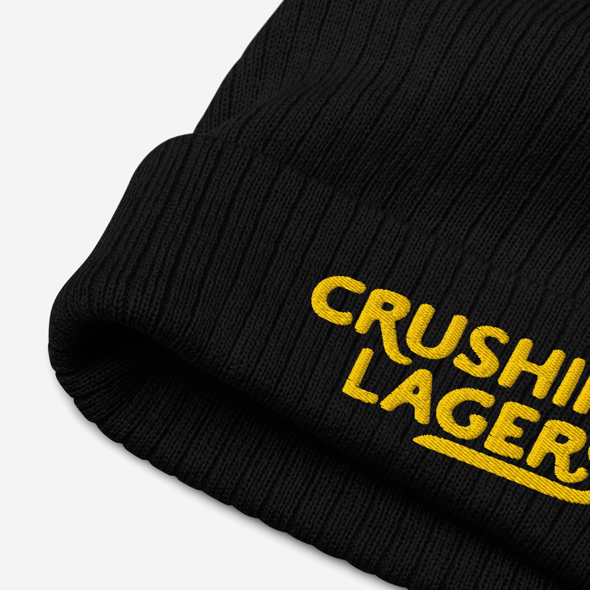 Close-up of the Crushin' Lagers Hat, a black rib-knit beanie featuring yellow CRUSHIN LAGER embroidery, showcasing its textured knit and raised stitching details.