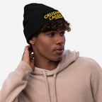 Young man wearing Crushin' Lagers Hat, a black knit beanie with yellow “CRUSHING LAGERS” text, paired with a light-tan hoodie. Perfect for lager enthusiasts, embodying casual style and good vibes.